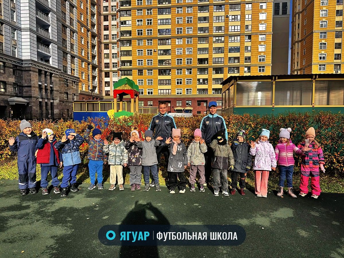 Девочки и мальчики из группы «Ягуара» с двумя тренерами машут руками на площадке во дворе
